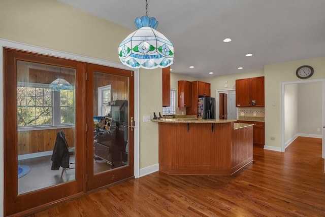 kitchen with pendant lighting, a breakfast bar, black fridge, dark hardwood / wood-style flooring, and kitchen peninsula