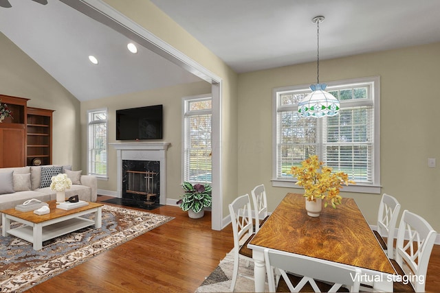 dining area with a premium fireplace, a healthy amount of sunlight, lofted ceiling, and hardwood / wood-style flooring