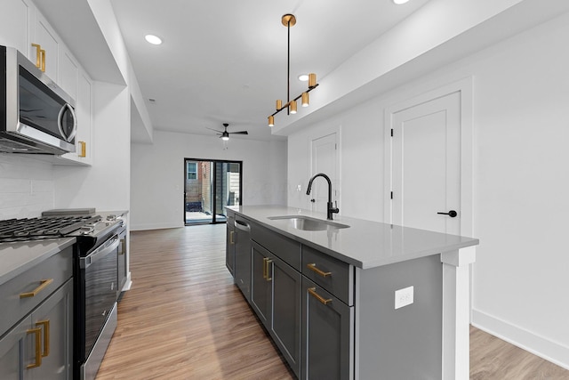 kitchen with pendant lighting, sink, stainless steel appliances, white cabinets, and a center island with sink