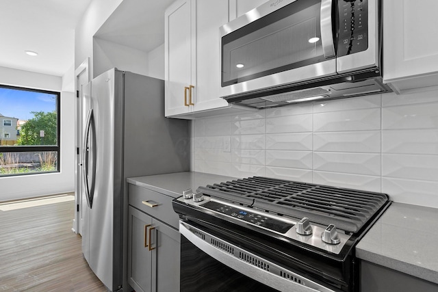 kitchen featuring stainless steel appliances, light wood-type flooring, white cabinets, and backsplash