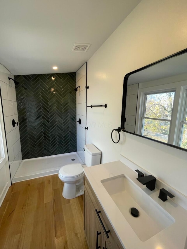 bathroom with hardwood / wood-style flooring, vanity, toilet, and tiled shower