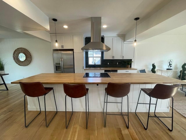 kitchen featuring ventilation hood, hanging light fixtures, light wood-type flooring, white cabinetry, and stainless steel appliances