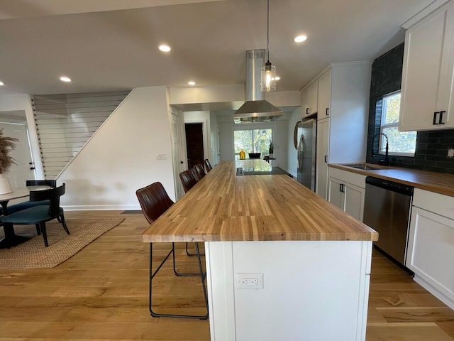 kitchen with sink, butcher block countertops, island range hood, a breakfast bar, and appliances with stainless steel finishes