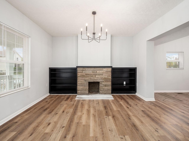 unfurnished living room featuring a fireplace, a textured ceiling, hardwood / wood-style flooring, and an inviting chandelier