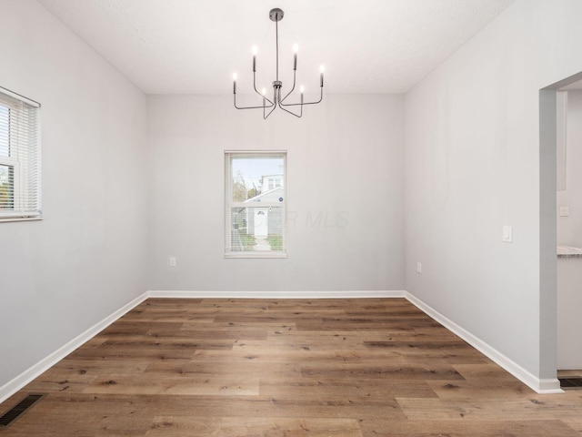 unfurnished dining area featuring hardwood / wood-style floors, an inviting chandelier, and a wealth of natural light