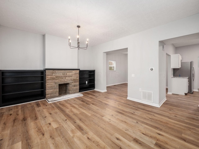 unfurnished living room with a chandelier, a textured ceiling, light hardwood / wood-style floors, and a fireplace