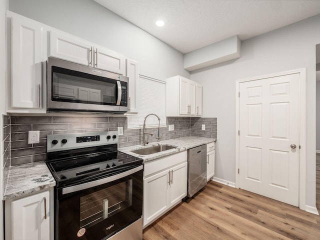 kitchen with sink, white cabinets, light hardwood / wood-style flooring, and appliances with stainless steel finishes