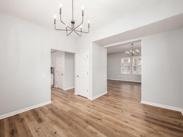 unfurnished dining area with hardwood / wood-style floors, a textured ceiling, and an inviting chandelier