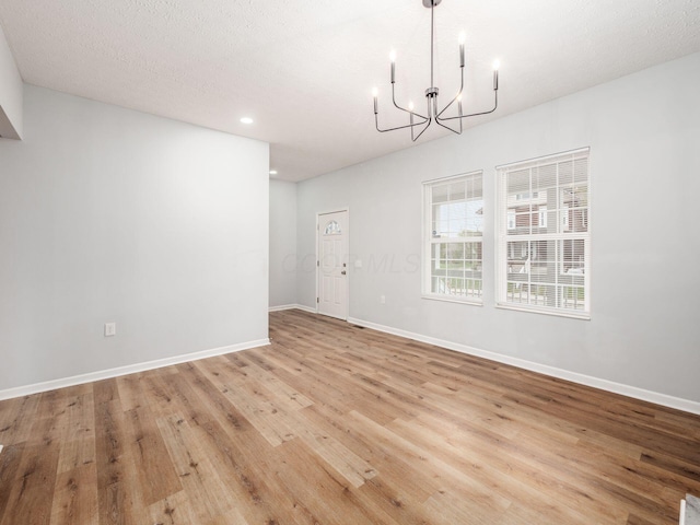 unfurnished dining area featuring a chandelier, a textured ceiling, and light hardwood / wood-style floors