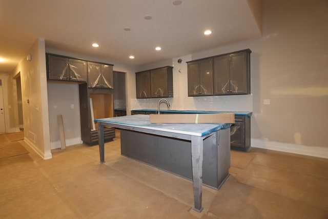 kitchen featuring backsplash, a kitchen island with sink, and sink