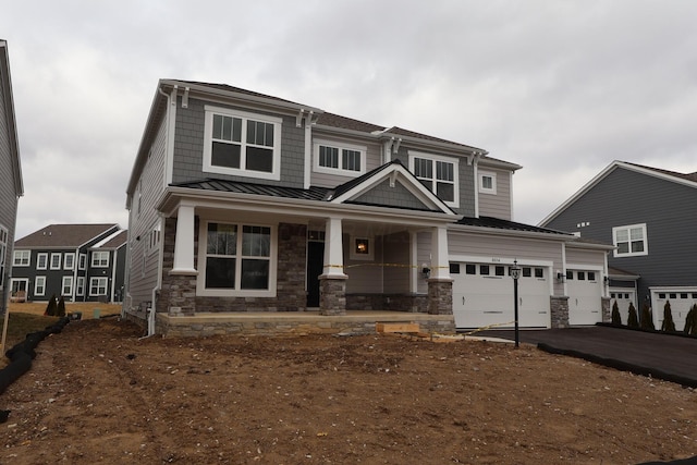 view of front of home featuring a standing seam roof, stone siding, covered porch, and driveway