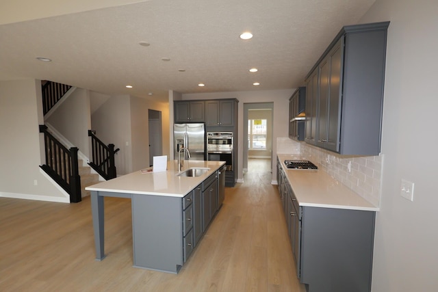 kitchen featuring a center island with sink, a sink, backsplash, appliances with stainless steel finishes, and light wood finished floors