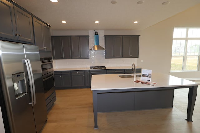 kitchen with a sink, light countertops, appliances with stainless steel finishes, wall chimney range hood, and tasteful backsplash