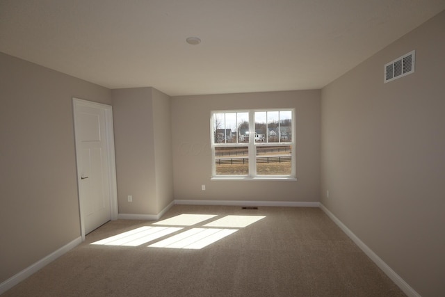 empty room featuring light colored carpet, visible vents, and baseboards