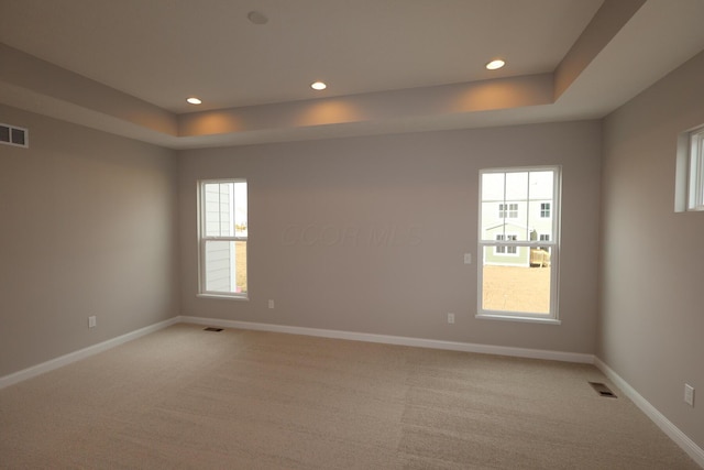 spare room featuring visible vents, a raised ceiling, and baseboards