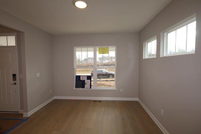 spare room with a wealth of natural light, visible vents, baseboards, and wood finished floors