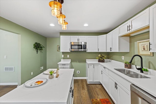 kitchen featuring stainless steel appliances, sink, dark hardwood / wood-style floors, white cabinetry, and hanging light fixtures