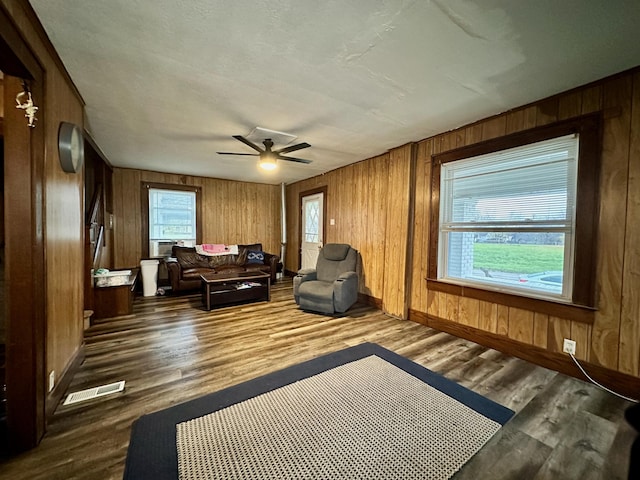 living area featuring wooden walls, dark hardwood / wood-style flooring, and ceiling fan