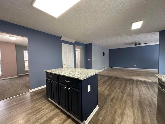 kitchen featuring ceiling fan, light stone counters, dark hardwood / wood-style flooring, a textured ceiling, and a kitchen island