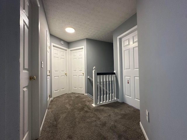 corridor featuring a textured ceiling and dark colored carpet