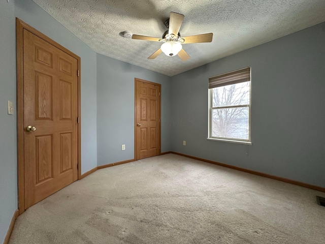 unfurnished bedroom featuring light carpet, a textured ceiling, and ceiling fan