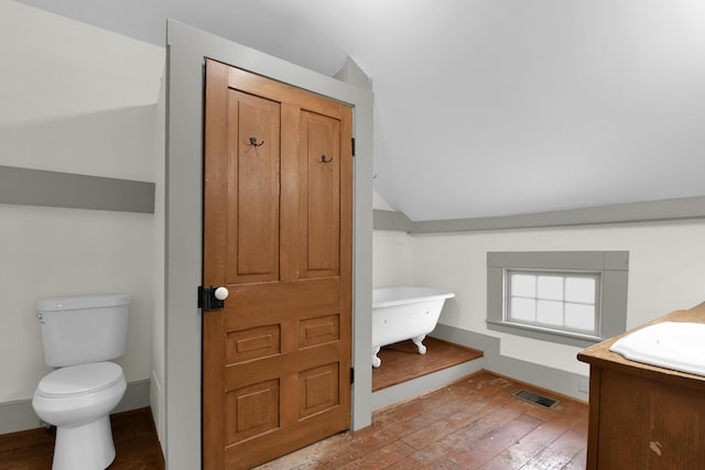 bathroom featuring lofted ceiling, hardwood / wood-style flooring, toilet, and a tub