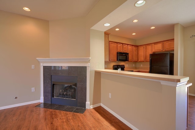 kitchen with black appliances, kitchen peninsula, a breakfast bar area, and hardwood / wood-style flooring