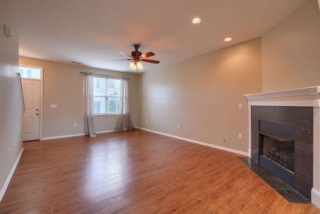 unfurnished living room featuring a tile fireplace, dark hardwood / wood-style floors, and ceiling fan