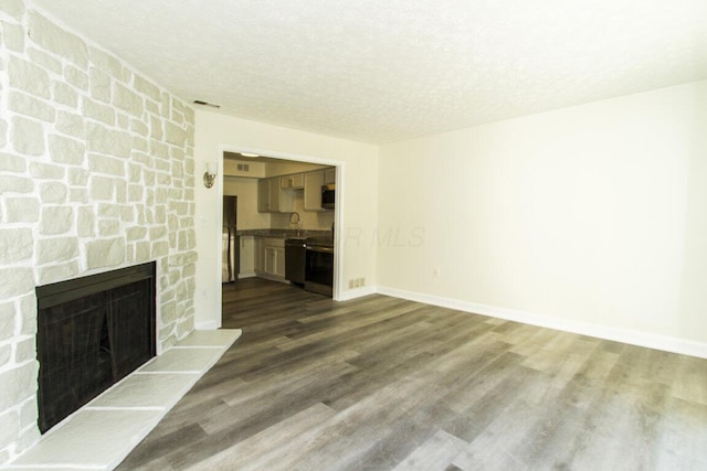 unfurnished living room with a textured ceiling, sink, a stone fireplace, and dark wood-type flooring