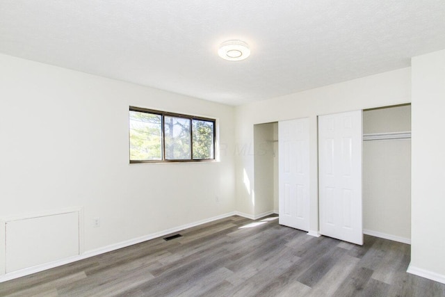 unfurnished bedroom featuring a textured ceiling, dark hardwood / wood-style flooring, and two closets