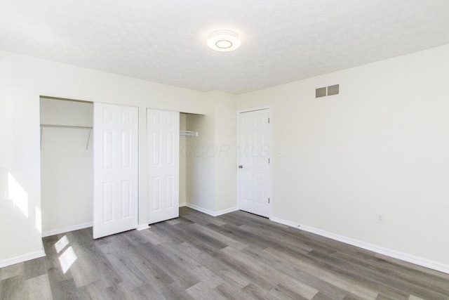 unfurnished bedroom with a textured ceiling, dark wood-type flooring, and two closets