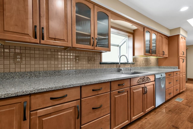 kitchen with decorative backsplash, light stone counters, stainless steel dishwasher, sink, and hardwood / wood-style flooring