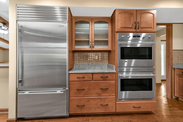 kitchen featuring decorative backsplash, hardwood / wood-style floors, light stone counters, and appliances with stainless steel finishes