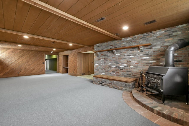 unfurnished living room featuring a wood stove, wooden ceiling, beamed ceiling, wood walls, and carpet