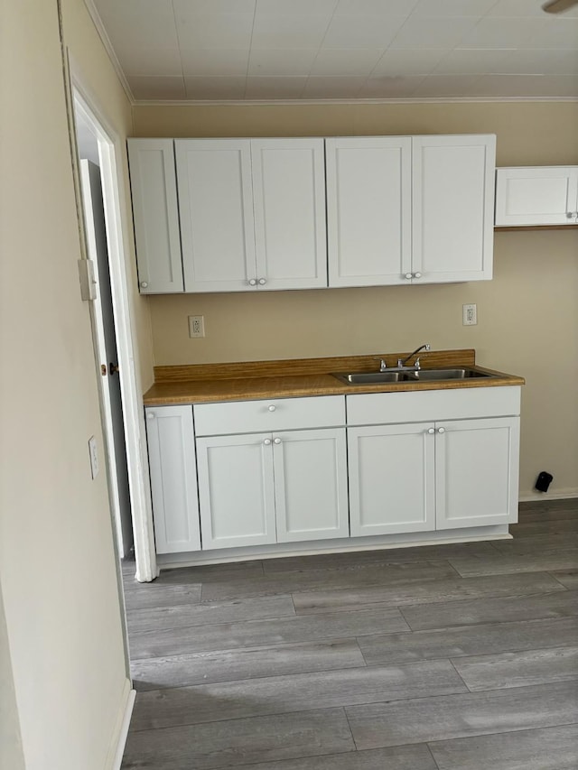 kitchen featuring sink, white cabinets, ornamental molding, and light wood-type flooring