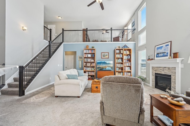 carpeted living room featuring a stone fireplace, a towering ceiling, and ceiling fan