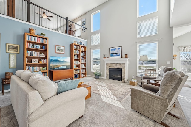 carpeted living room featuring a stone fireplace, a towering ceiling, and ceiling fan