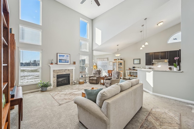 carpeted living room with a stone fireplace, ceiling fan, and a high ceiling