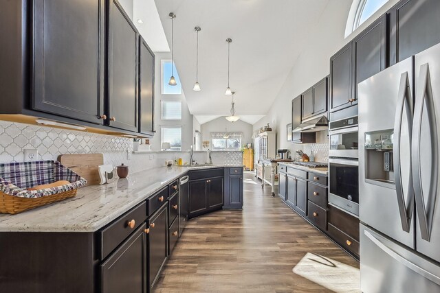 kitchen featuring pendant lighting, lofted ceiling, sink, stainless steel appliances, and light stone countertops