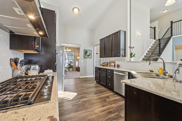 kitchen featuring sink, appliances with stainless steel finishes, dark brown cabinets, light stone countertops, and wall chimney exhaust hood