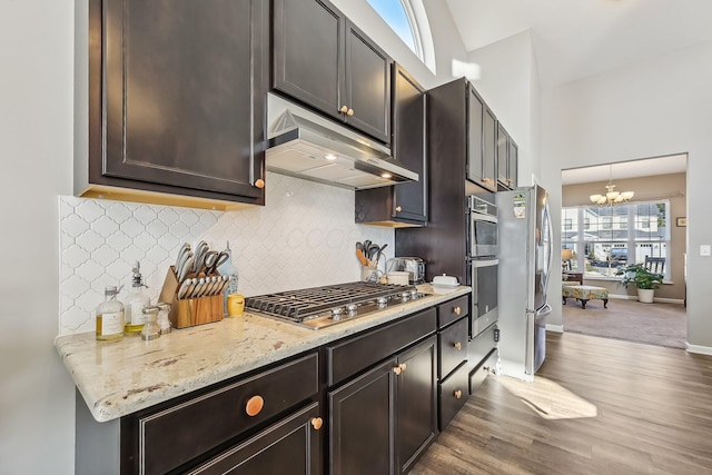 kitchen featuring dark brown cabinetry, a notable chandelier, pendant lighting, stainless steel appliances, and light stone countertops