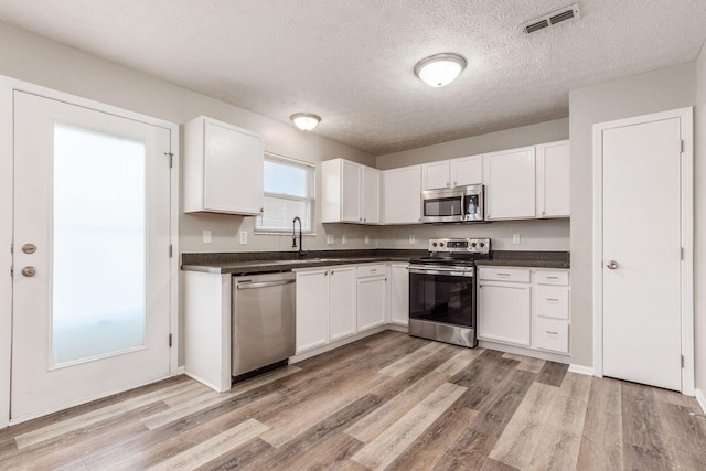 kitchen featuring white cabinets, light wood-type flooring, stainless steel appliances, and a textured ceiling