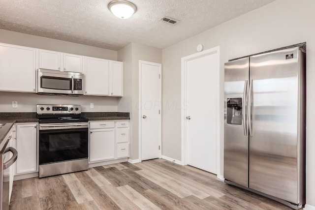 kitchen with a textured ceiling, white cabinetry, stainless steel appliances, and light hardwood / wood-style flooring