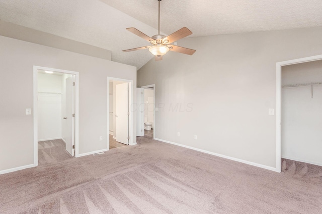 unfurnished bedroom featuring light carpet, a spacious closet, vaulted ceiling, and ceiling fan