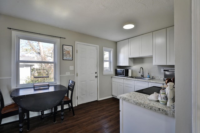 kitchen featuring light stone countertops, a textured ceiling, dark wood-type flooring, sink, and white cabinetry