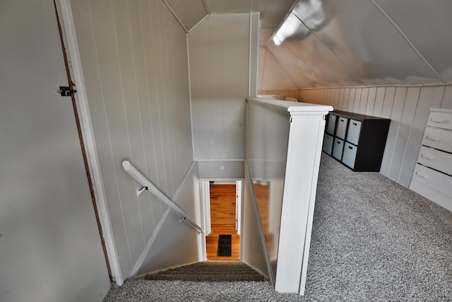 stairway with carpet, wooden walls, and lofted ceiling