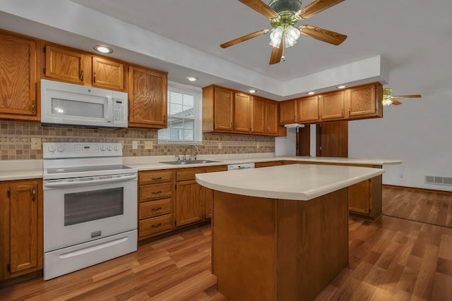 kitchen featuring a sink, white appliances, wood finished floors, and brown cabinetry