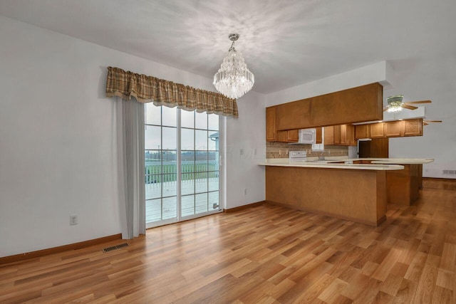 kitchen featuring pendant lighting, ceiling fan with notable chandelier, decorative backsplash, light hardwood / wood-style floors, and kitchen peninsula