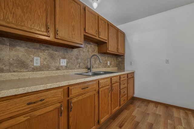 kitchen featuring light wood-type flooring, a sink, brown cabinetry, light countertops, and decorative backsplash