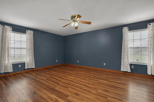 empty room featuring ceiling fan, dark wood-type flooring, a healthy amount of sunlight, and a textured ceiling